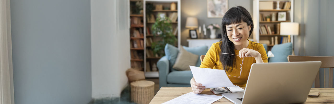 person on laptop and holding a document at home