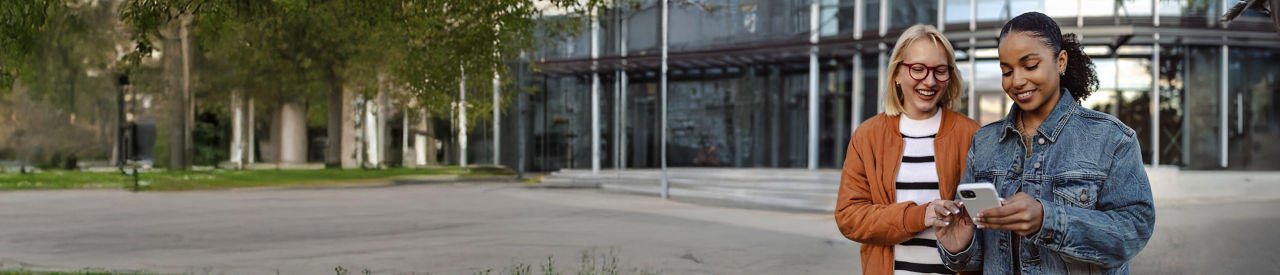 two adults smiling and looking at mobile device outside