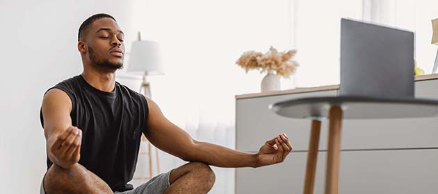 man closing his eyes and meditating at home with laptop