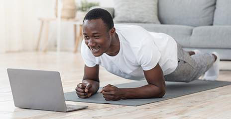 Male is doing a plank in front of his laptop