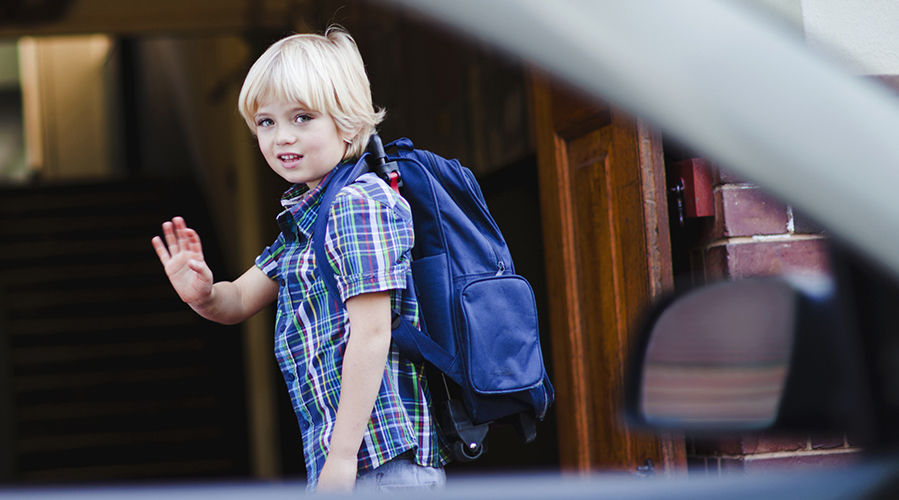 niño pequeño con mochila despidiéndose antes de ir a la escuela y sonriendo