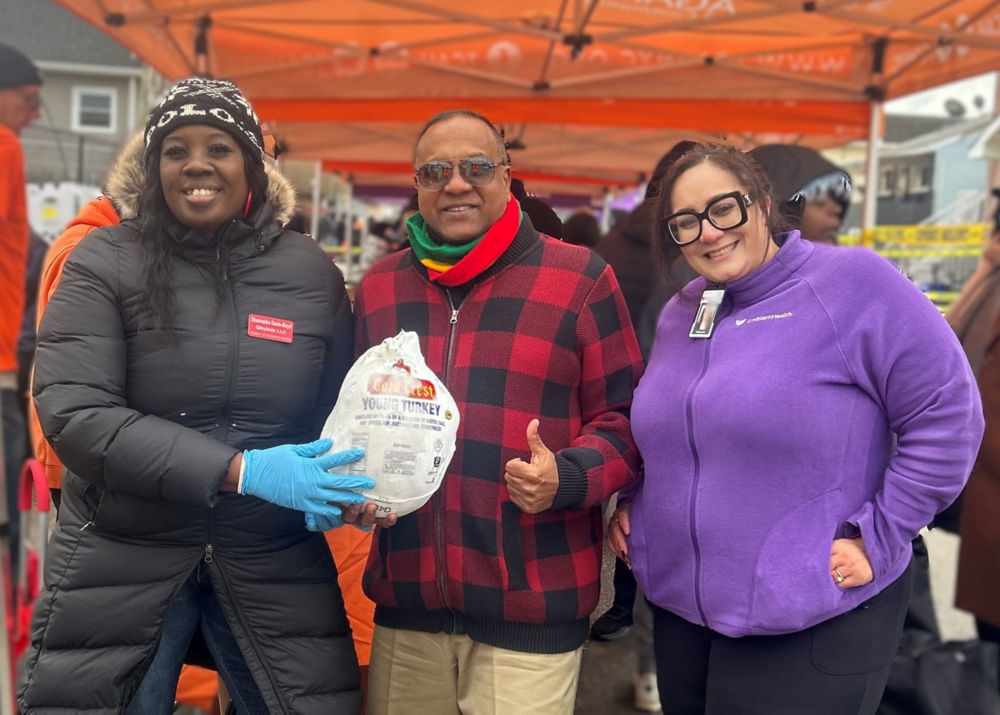 Miembro de la comunidad y personal de EmblemHealth en una distribución de alimentos navideña. 