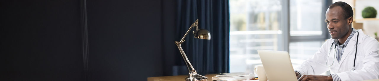 A male doctor is working on his laptop at a desk. 