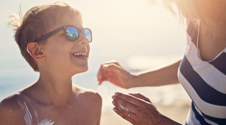 mother applying sunscreen on her son at the beach