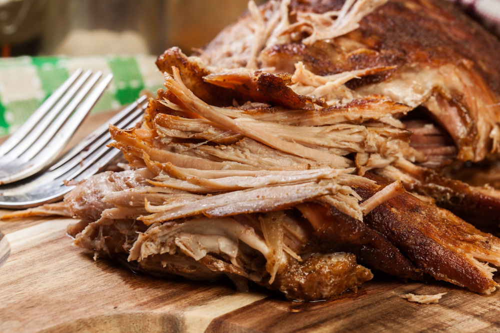 Pulled pork on wood cutting board next to two forks.