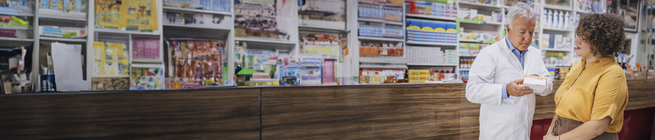 Hombre mayor con barba hablando con una farmacéutica.