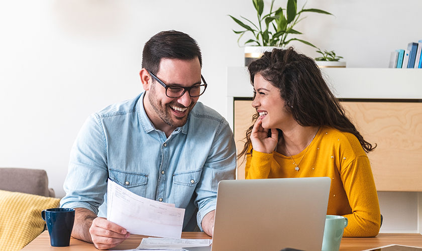 Happy husband and wife read good news online at laptop, smiling man holding documents receiving positive decision from bank