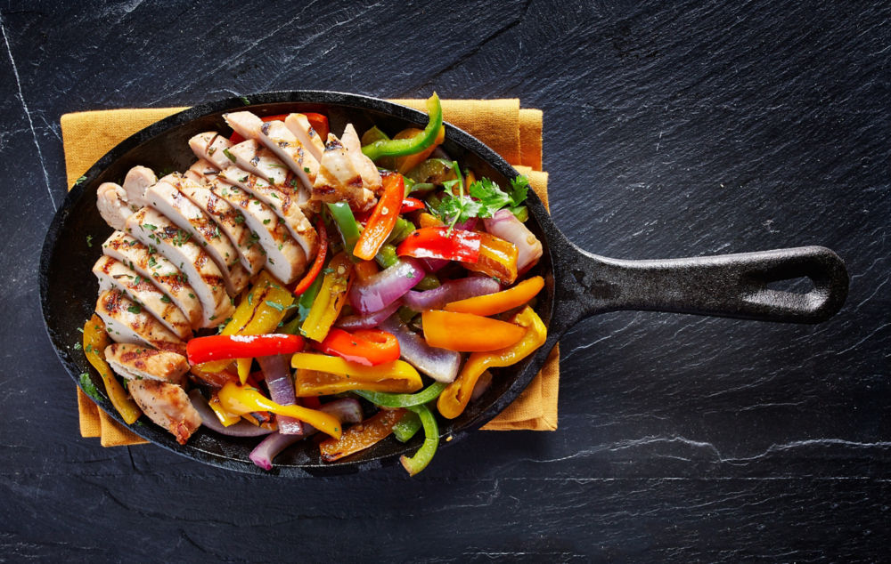 fajitas mexicanas de pollo a la parrilla en sartén de hierro fotografiadas desde arriba sobre losa oscura