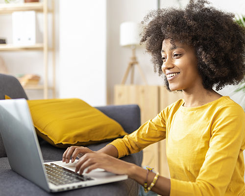 Mujer joven feliz usando una computadora portátil cerca al sofá en casa