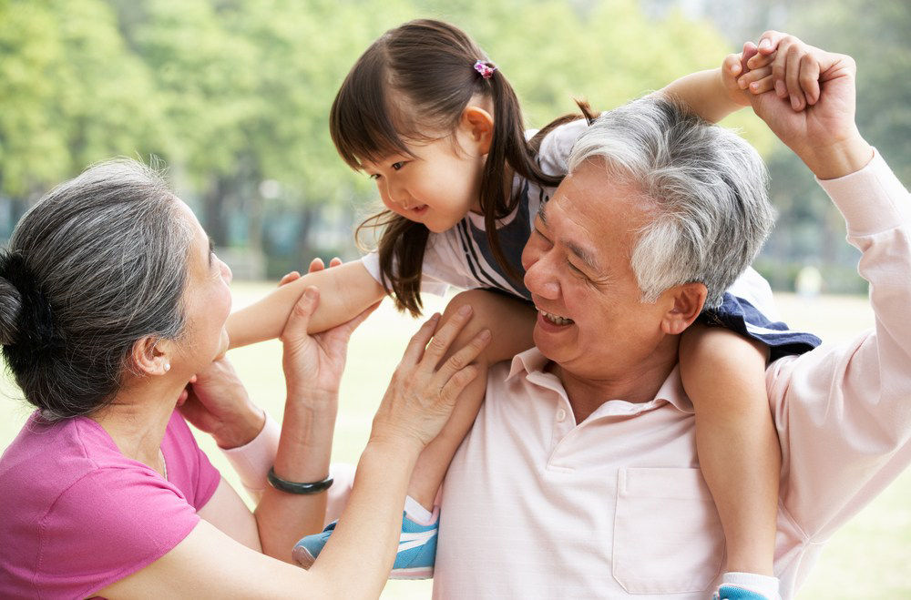 Niña sobre los hombros de su abuelo sonriendo a su abuela.