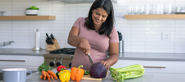 mujer adulta joven corta verduras en la cocina y sonríe