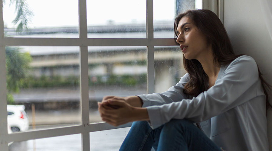 mujer joven mirando por la ventana en su hogar durante un día lluvioso.