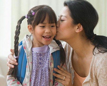 young mother kissing daughter before school