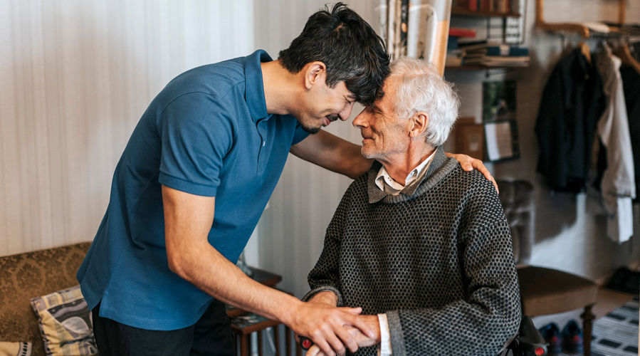 Un cuidador masculino sosteniendo la mano de un hombre anciano, brindando apoyo y consuelo.