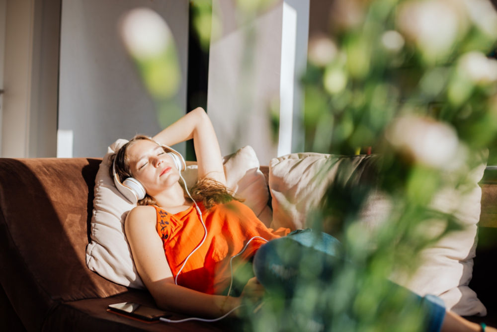 Mujer relajándose bajo la luz del sol, escuchando música, bajo techo.