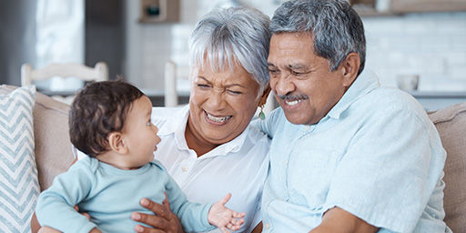 happy senior couple holding grandchild and sitting on couch