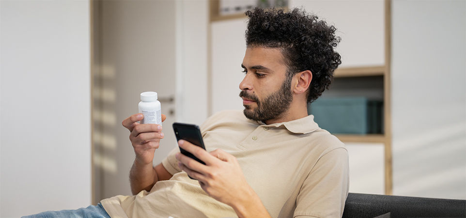 hombre mirando un frasco de píldoras y sosteniendo un teléfono celular