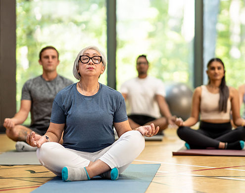 Un grupo diverso de adultos medita en sus colchonetas de yoga en un gimnasio. 