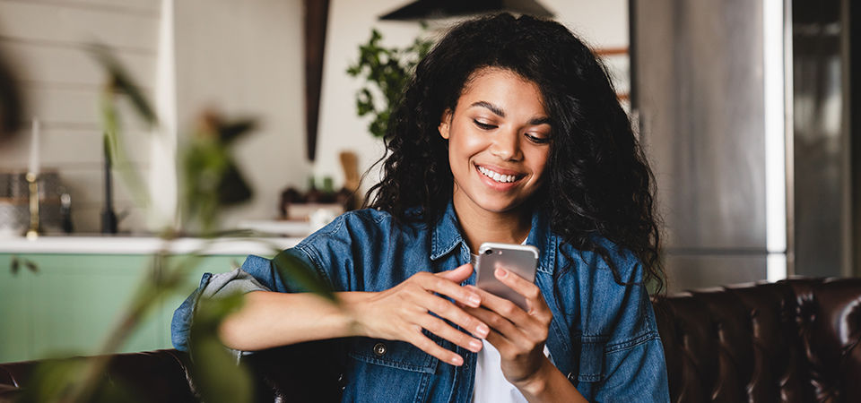 Relaxed young african woman texting on her phone in the modern house.Smiling african american woman using smartphone at home, messaging or browsing social networks while relaxing on couch