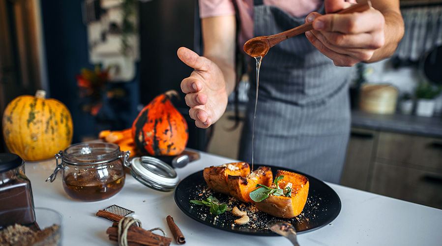 Un joven en una cocina rústica preparando y sirviendo un postre saludable. Calabaza con canela y miel.