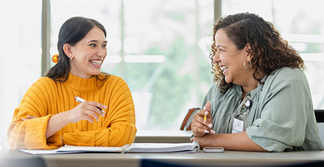 A happy sales person talking to customer and sitting at a table with notebook