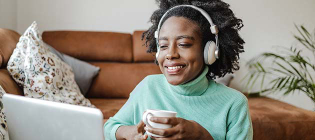 mujer sonriente con auriculares mira una computadora portátil y sostiene una bebida