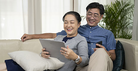 asian couple smiling and looking at computer on couch