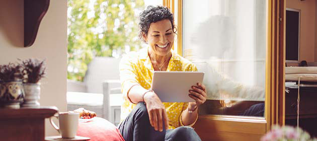 smiling woman sitting by window and looking at tablet