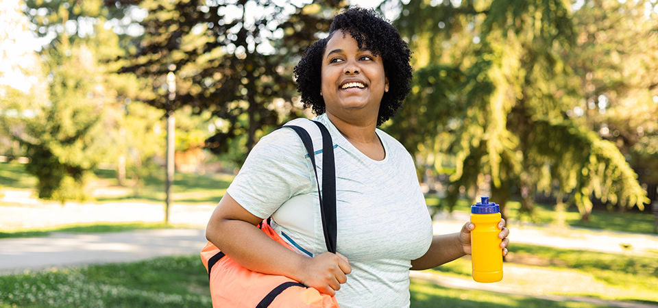 woman holding a yoga mat and water bottle in park