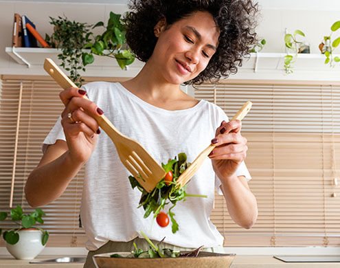 Mujer multirracial joven y feliz mezclando un bol de ensalada fresca. 