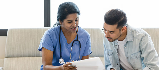 A young man and female primary care provider sitting on office couch and reviewing a medical chart together.