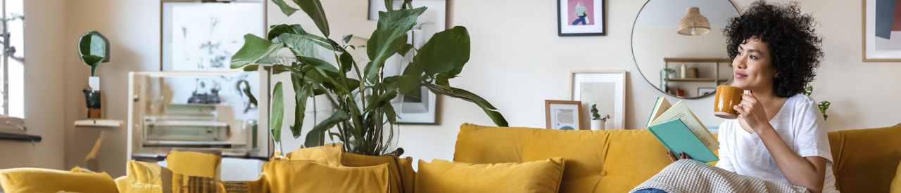 woman drinking coffee and reading a book on yellow couch 