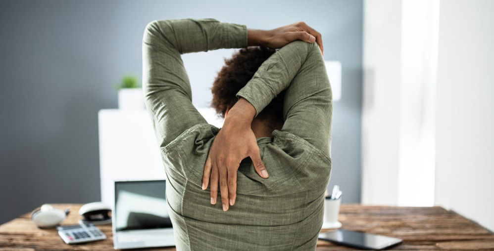 Persona en la mesa con computadora portátil, estirando los brazos por encima de la cabeza.