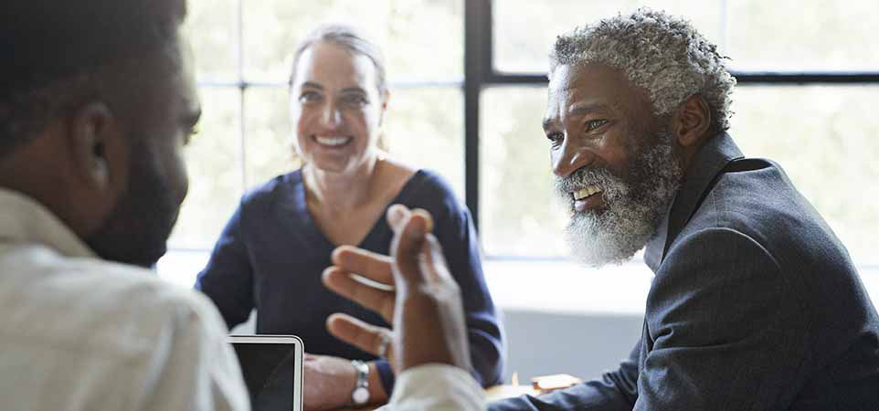 Smiling businessman looking at coworker while sitting in board room during office meeting